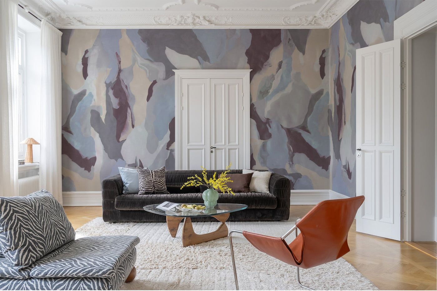blue wall mural on the walls fo this living room. dark brown velvet sofa , wooden floor, white rugg