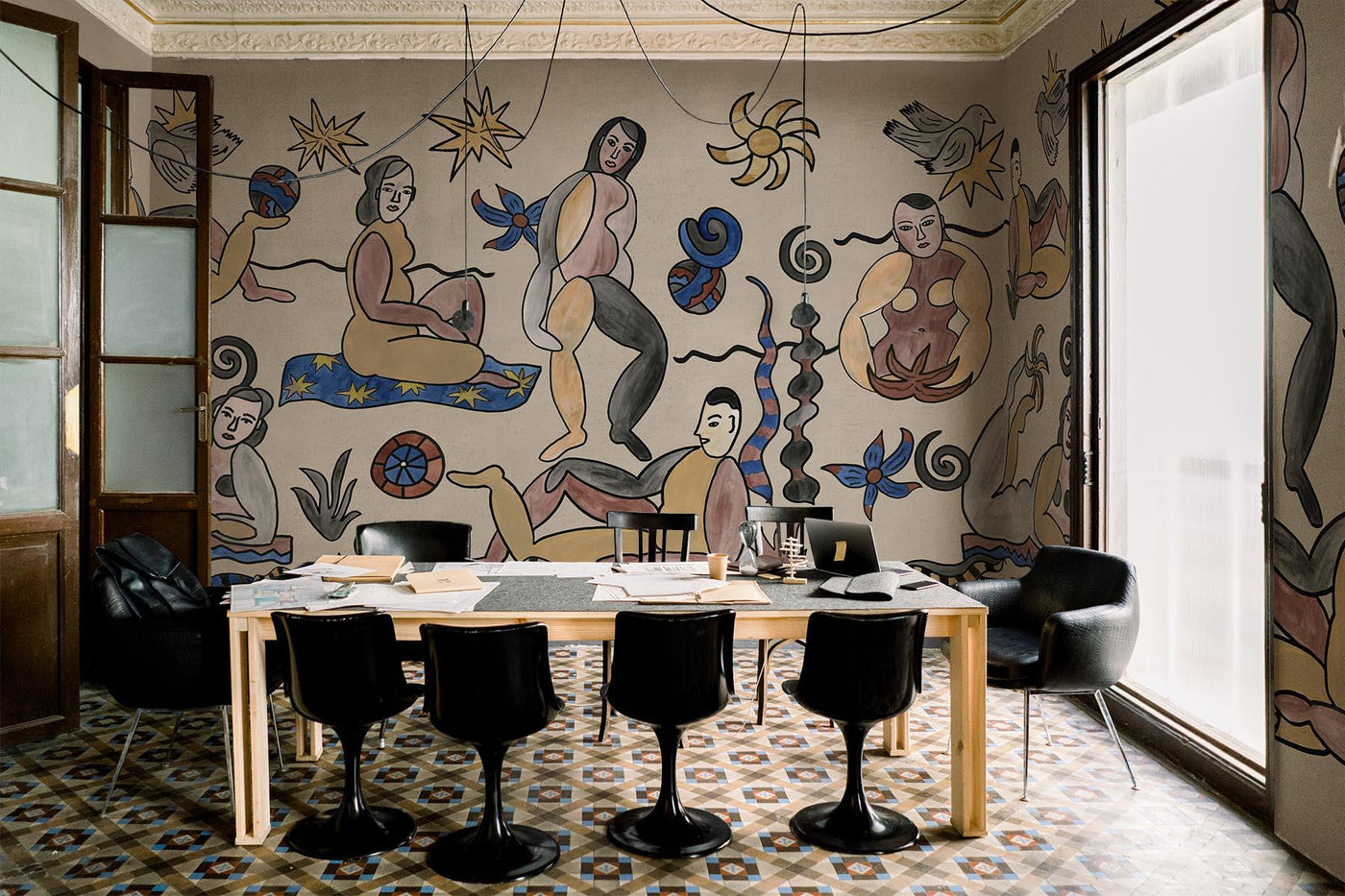 beige artistic wall mural on the walls of this dining room. ceramic floor with a mediterranean pattern on the floor. Wooden table and black plastic chairs