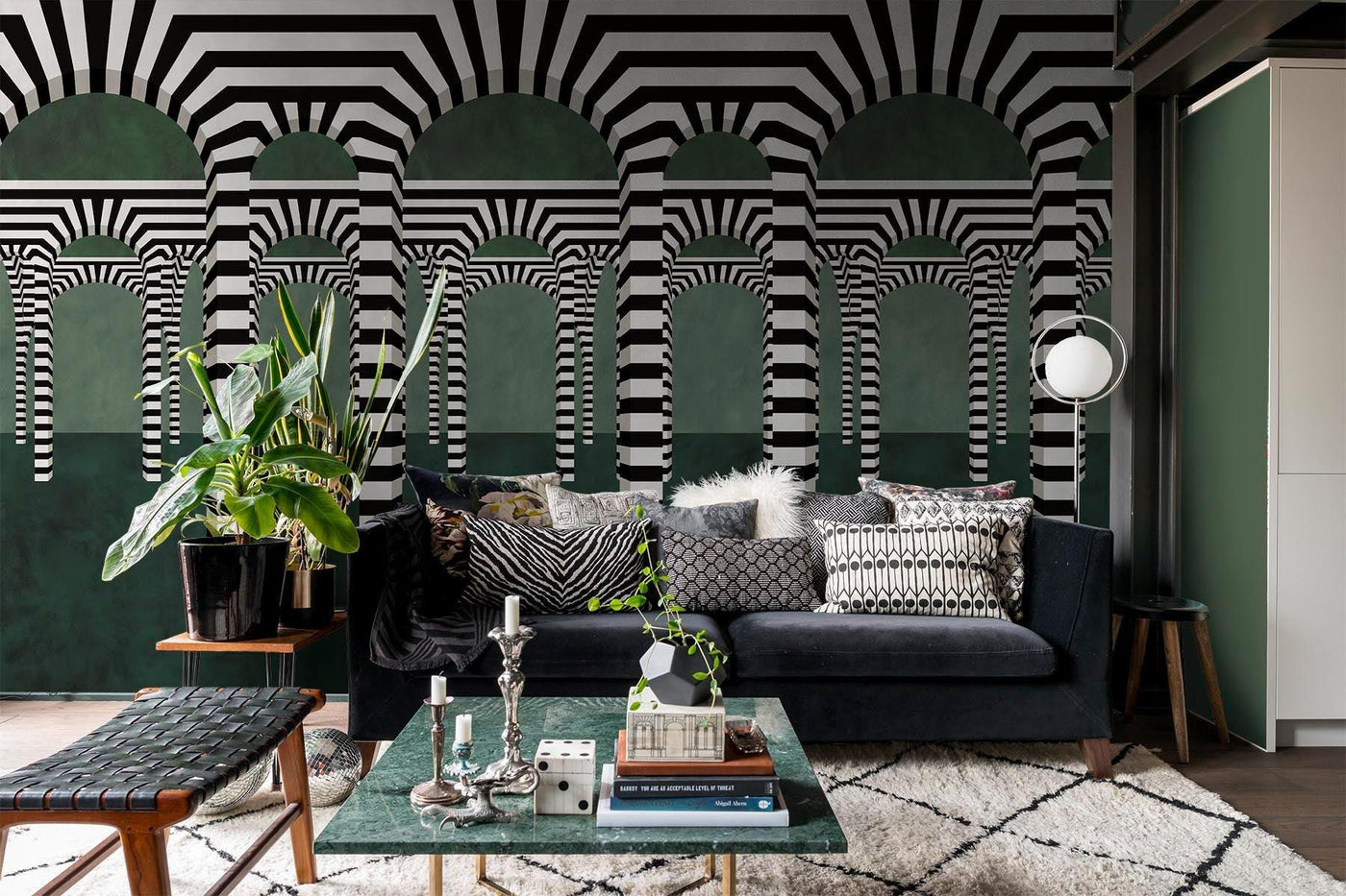 Djärv svartvit valvvägg väggmålning i grönt på vardagsrumets vägg bakom den grå soffan. Kvadratglasbord och en leteringsbänk i svart på sidan. Vit matta med svart Argile -motiv på trägolvet