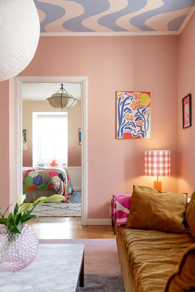 Blue Curved wall mural in the ceiling of Hanna Mw´s pink living room. Mustard colored sofa. Pastel colored layered rugg. marble table